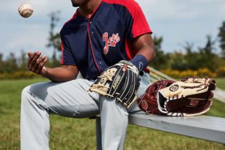 A baseball player sits on a bench next to a variety of gloves