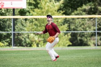 A baseball player awaits a fly ball in the outfield.