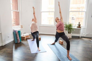Two women perform crescent lunges indoors.