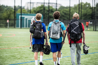Three lacrosse players walk with their bags