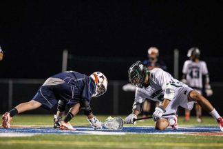 Two lacrosse players compete in a faceoff.