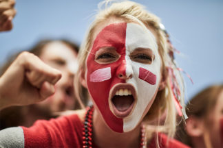 blonde woman with red and white facepaint cheering on her team at a game