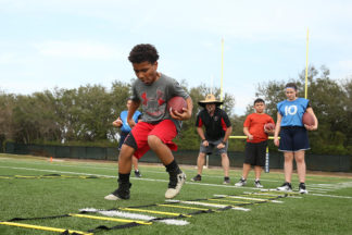 younger football player at practice using agility drill ladder