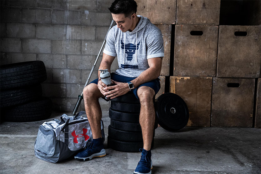 man at gym sitting on weights with Under Armor gym bag and water bottle