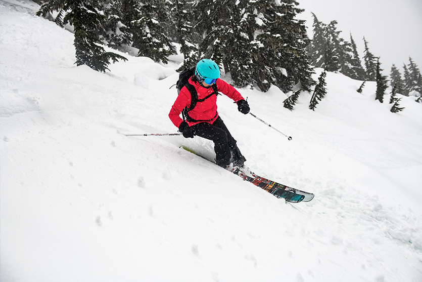 person skiing wearing red ski jacket and teal ski helmet