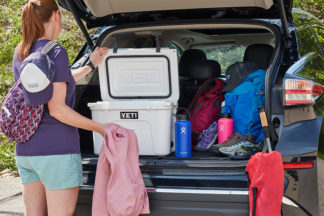 Woman Packing YETI Cooler In Trunk Of Car With Various Other Camping Gear