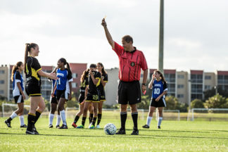 Soccer referee holding a yellow card during a girls soccer game