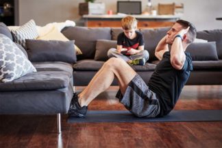 Dad Doing Sit-ups At Home While Child Sits On Couch