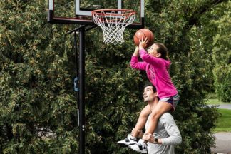 dad lifts daughter up who is holding basketball to shoot in basketball hoop