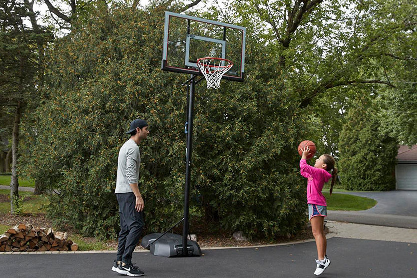 father rand daughter shooting a basketball in their driveway at a portable basketball hoop