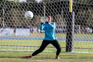 soccer goalkeeper makes save on soccer field with blue soccer goalkeeper shirt and goalkeeper gloves