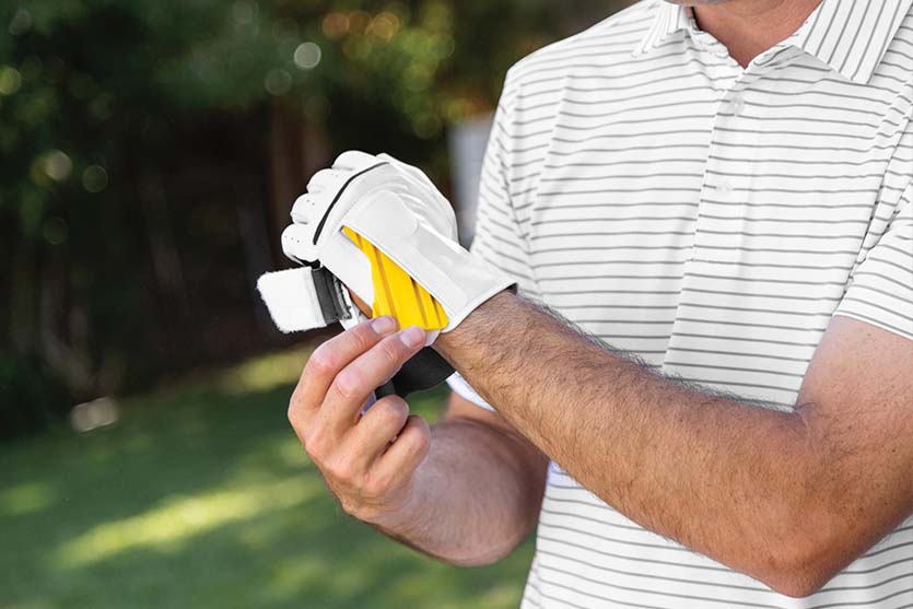 man fastens golf training aid glove before taking to the golf course