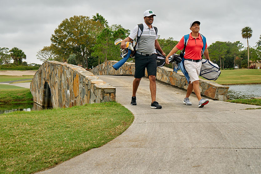 Two Golfers Walking On Golf Course And Carrying Golf Bags