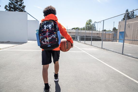 young kid wearing a backpack on a basketball court