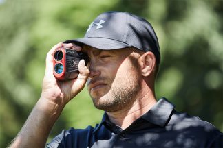 Image features a man looking through a golf rangefinder.
