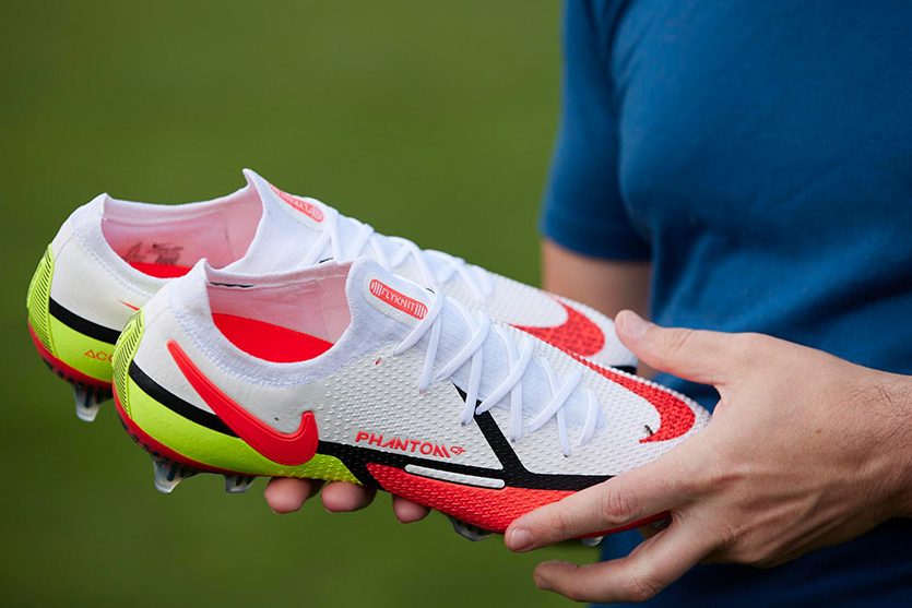 A soccer player holding a pair of Nike Phantom GT2 Elite FG Soccer Cleats.